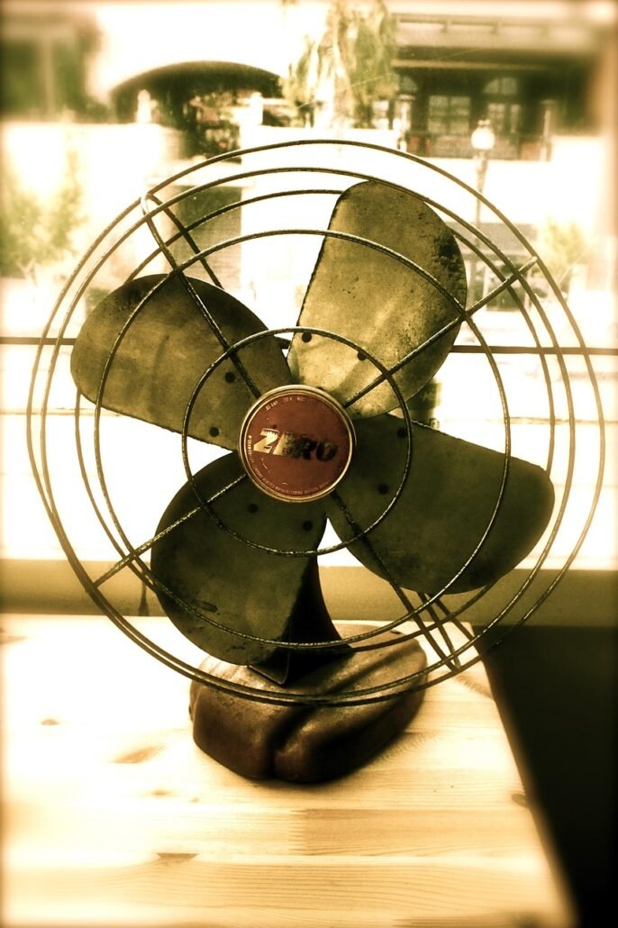 electric fan blowing air toward large duvet hanging indoors