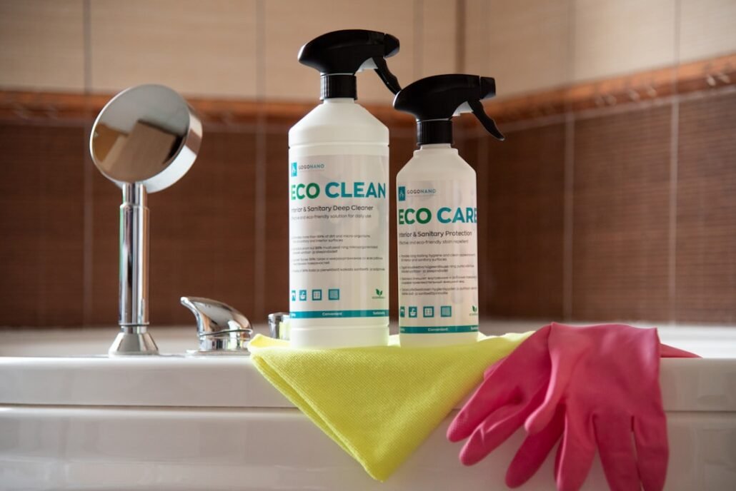 bathroom cleaning supplies laid out on floor — grout cleaner spray bottle, old toothbrush, rubber gloves