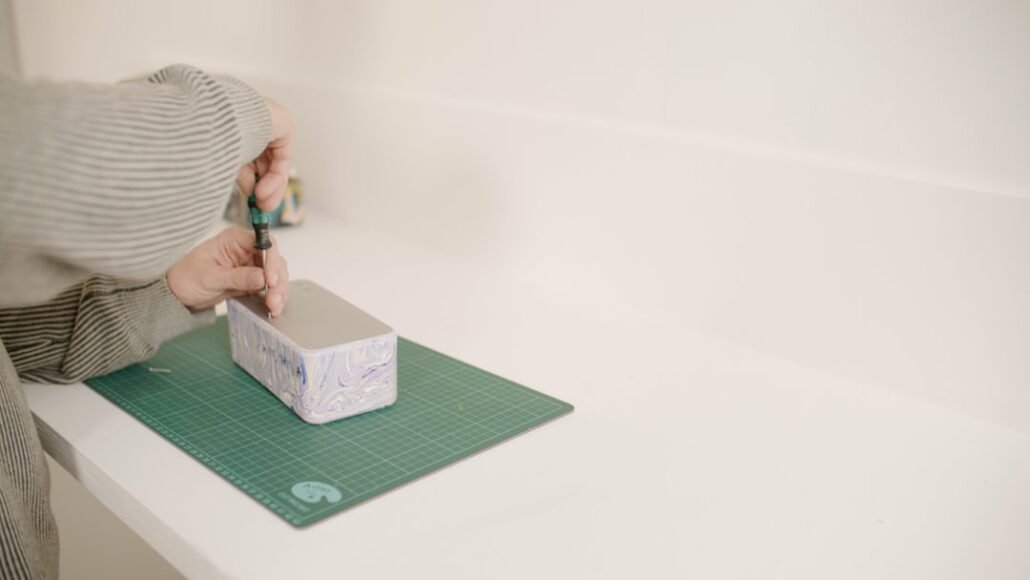 person decorating cardboard box with white adhesive paper to make it look like a store-bought storage box